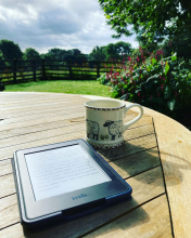 Kindle and mug in a sunny garden.